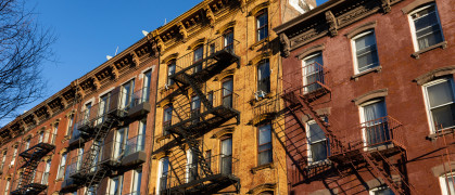 Looking up at a row of colorful old brick residential buildings with fire escapes along a street in Williamsburg Brooklyn of New York City